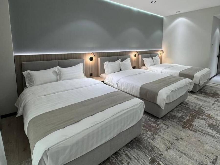 Ein modernes Hotelzimmer mit drei Betten, einem Holzkopfteil und einem grauen Teppich.