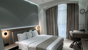 Un dormitorio moderno con una cama grande, mesitas de noche, un escritorio y un ventanal curvo con cortinas.