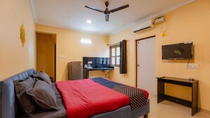 A bedroom with a bed, a desk, a television, and a ceiling fan. - New White Minar  (Calangute)