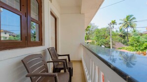 A balcony with two wooden chairs, a white railing, and a view of palm trees and greenery. - New White Minar  (Calangute)