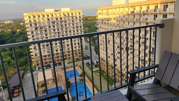 A balcony with a view of high-rise buildings, a swimming pool, and a clear sky.