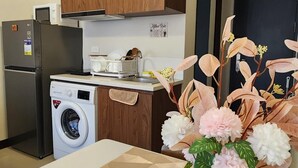 A modern kitchen with wooden cabinets, a washing machine, and a dining area with a table and decorative flowers.