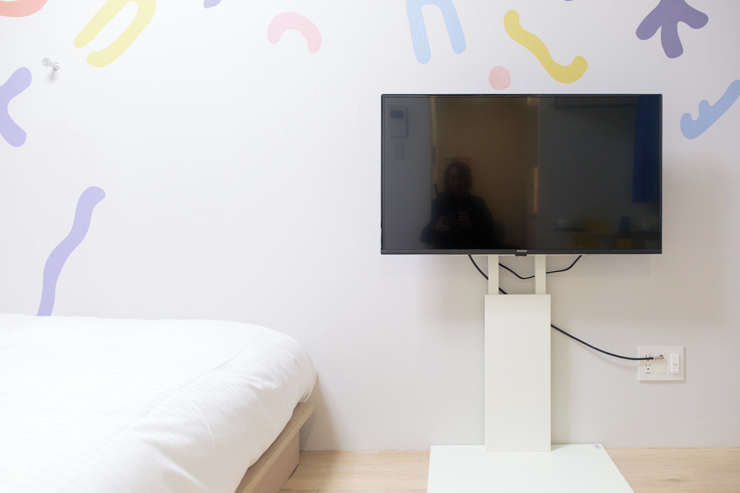 Un dormitorio con cama, televisor de pantalla plana en la pared y mesita de noche blanca.