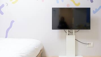 Un dormitorio con cama, televisor de pantalla plana en la pared y mesita de noche blanca.