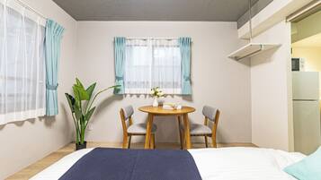 Habitación de hotel con cama, una mesa de comedor con dos sillas, una planta en maceta y una ventana con cortinas.