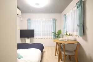 Una habitación de hotel con una cama, un televisor, una mesa con un libro y una silla.