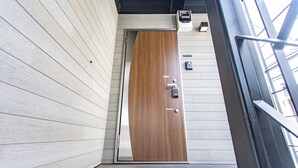 A modern hotel entrance with a wooden door, a keypad lock, and a small security camera. - Ars Garden Omori (Tokyo)