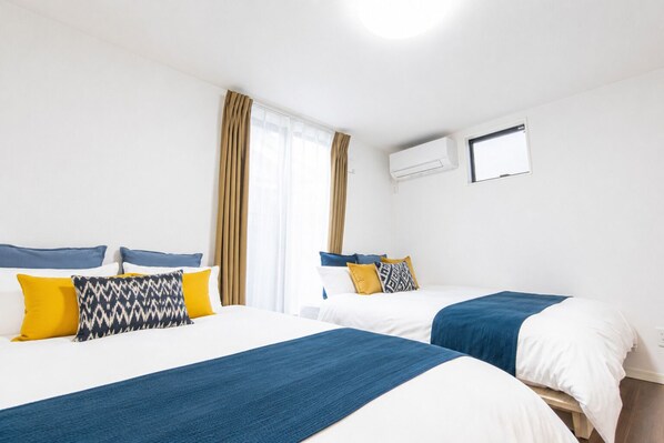 Habitación de hotel con dos camas, una ventana con cortinas, un equipo de aire acondicionado y un televisor montado en la pared.