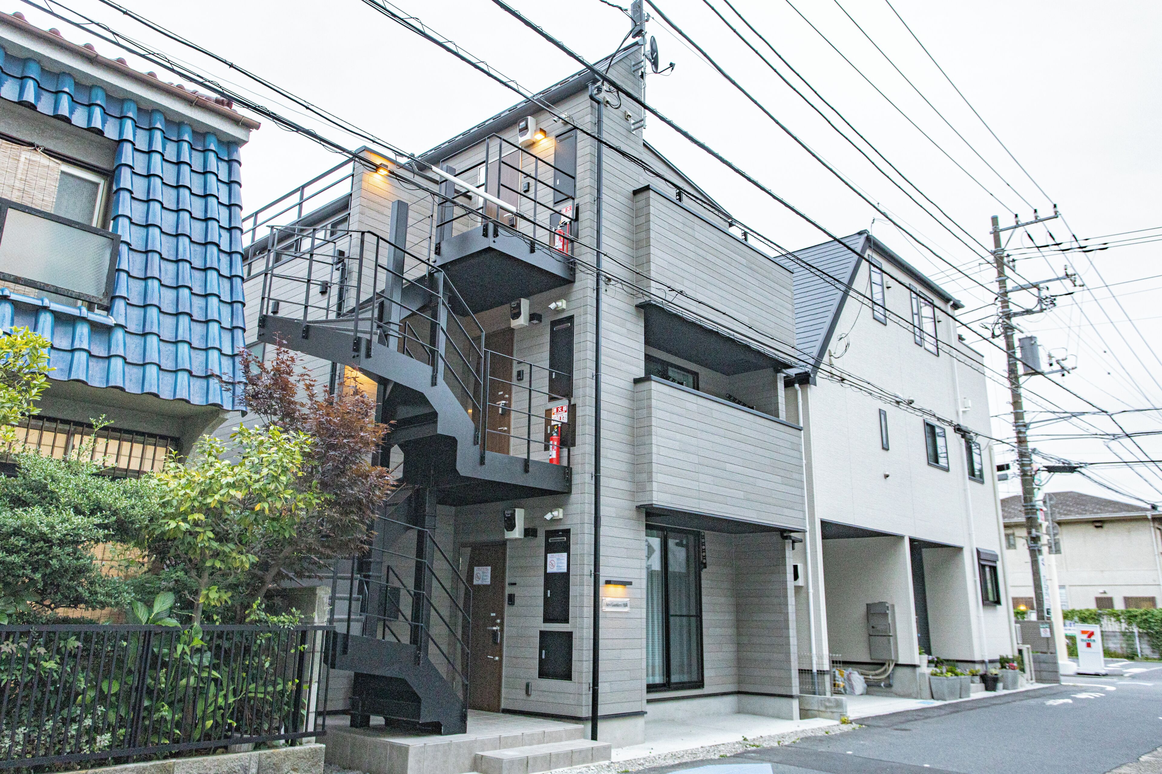 A modern two-story building with a metal staircase, a garage, and a small garden area.