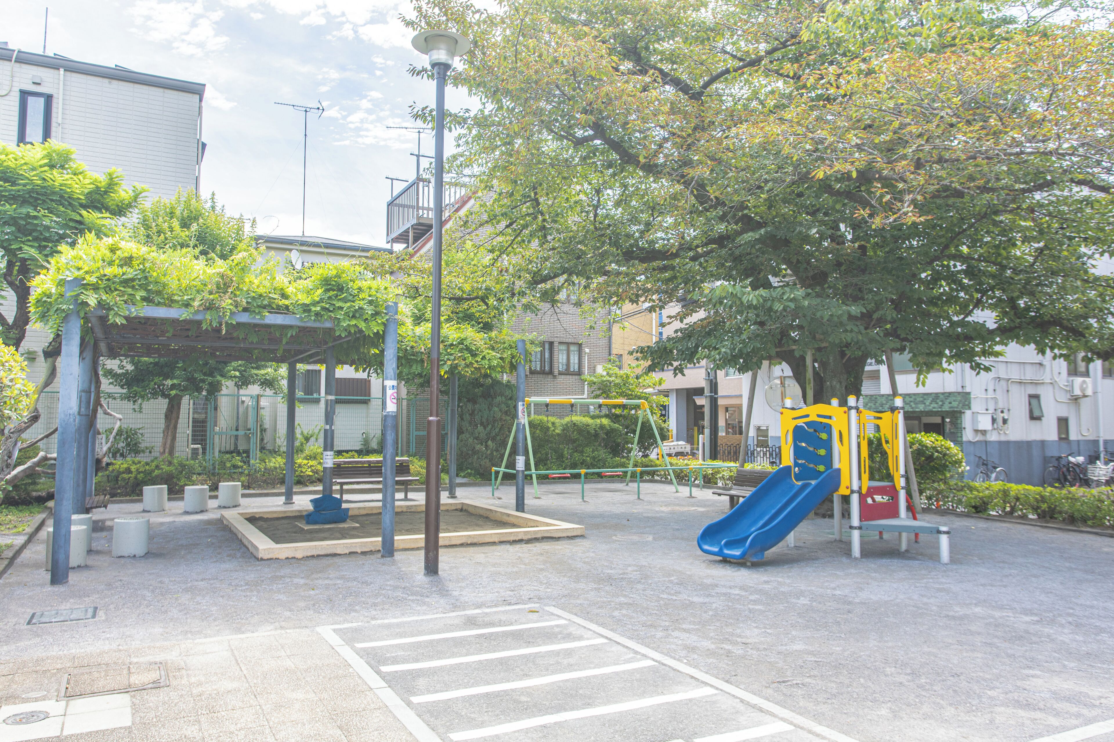 A playground with a slide and swings, surrounded by trees and buildings.