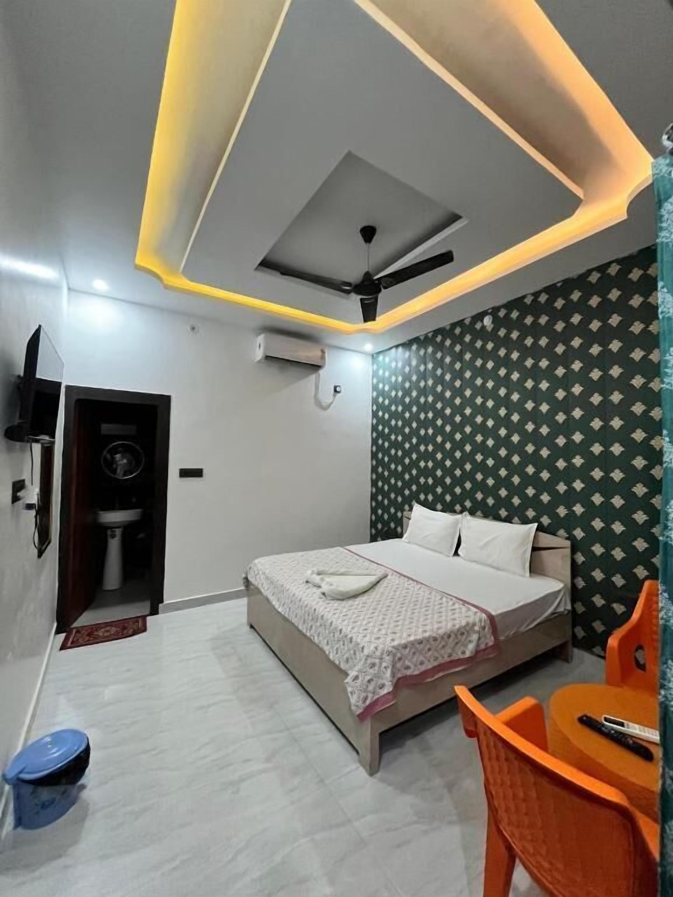 A modern bedroom with a bed, a ceiling fan, an air conditioning unit, a small table with a chair, and a patterned wall.
