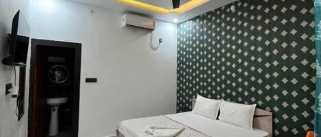 A modern bedroom with a bed, a ceiling fan, an air conditioning unit, a small table with a chair, and a patterned wall.