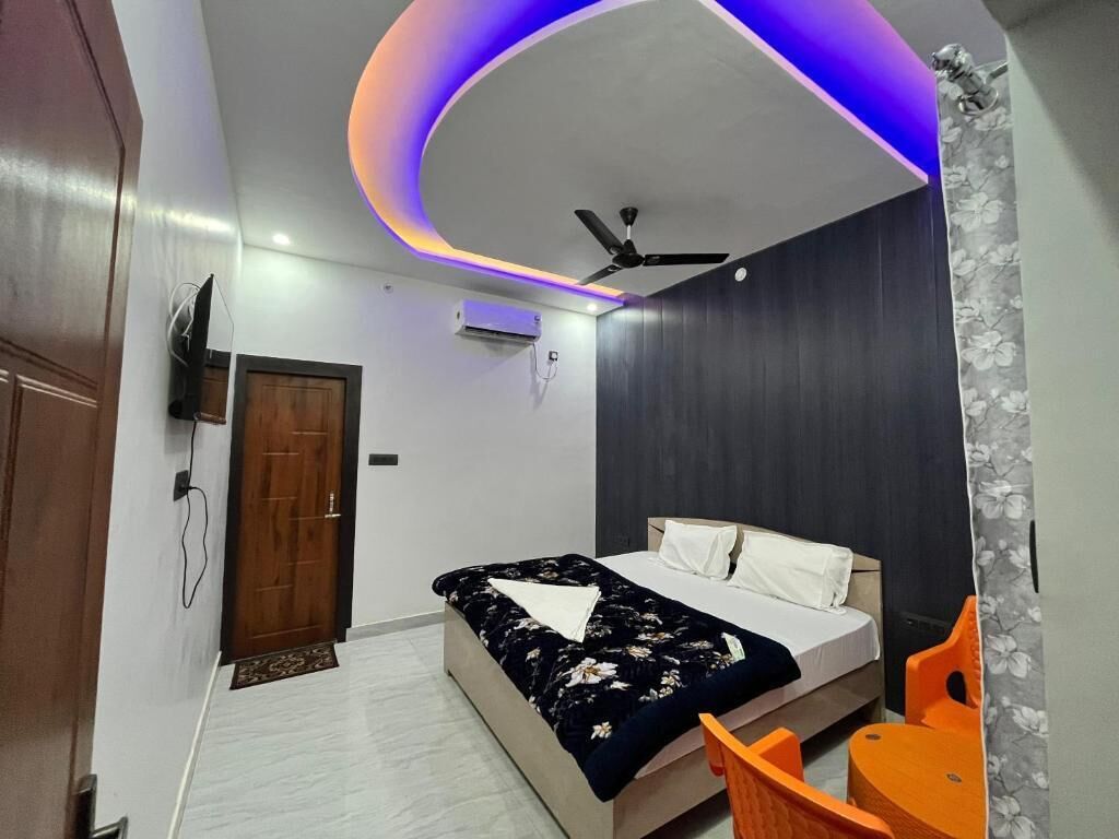 A bedroom with a bed, a ceiling fan, an air conditioning unit, and a TV mounted on the wall.
