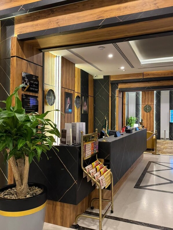 A modern reception area with a black marble counter, wooden accents, and a potted plant.