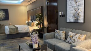 A modern hotel room with a bed, sofa, coffee table, and artwork. - SWAT SERVICED APARTMENTS 5 (Al Khobar)