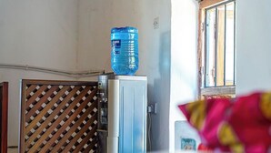 Eine kleine Küchenzeile mit Wasserspender, einer Tür mit Muster und einem Fenster mit Gitterstäben.
