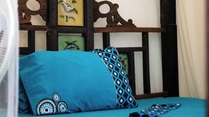 Ein Bett mit blauer Bettdecke und Kissen, ein Holz-Kopfteil mit Verzierungen und ein gerahmtes Bild an der Wand.