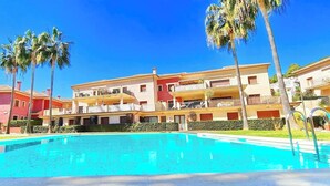 Un hotel con piscina, varios balcones y palmeras.