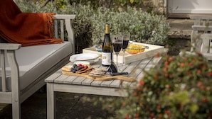 An outdoor dining area with a table set for two, featuring a bottle of wine, glasses, plates, and a basket of bread. - Elegant dog friendly home with panoramic views - The Old Vicarage (Aldsworth)