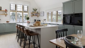 A modern kitchen with a large island, bar stools, and a dining table set for two. - Incredible dog friendly with hot tub - The Old Stores (Toddington)