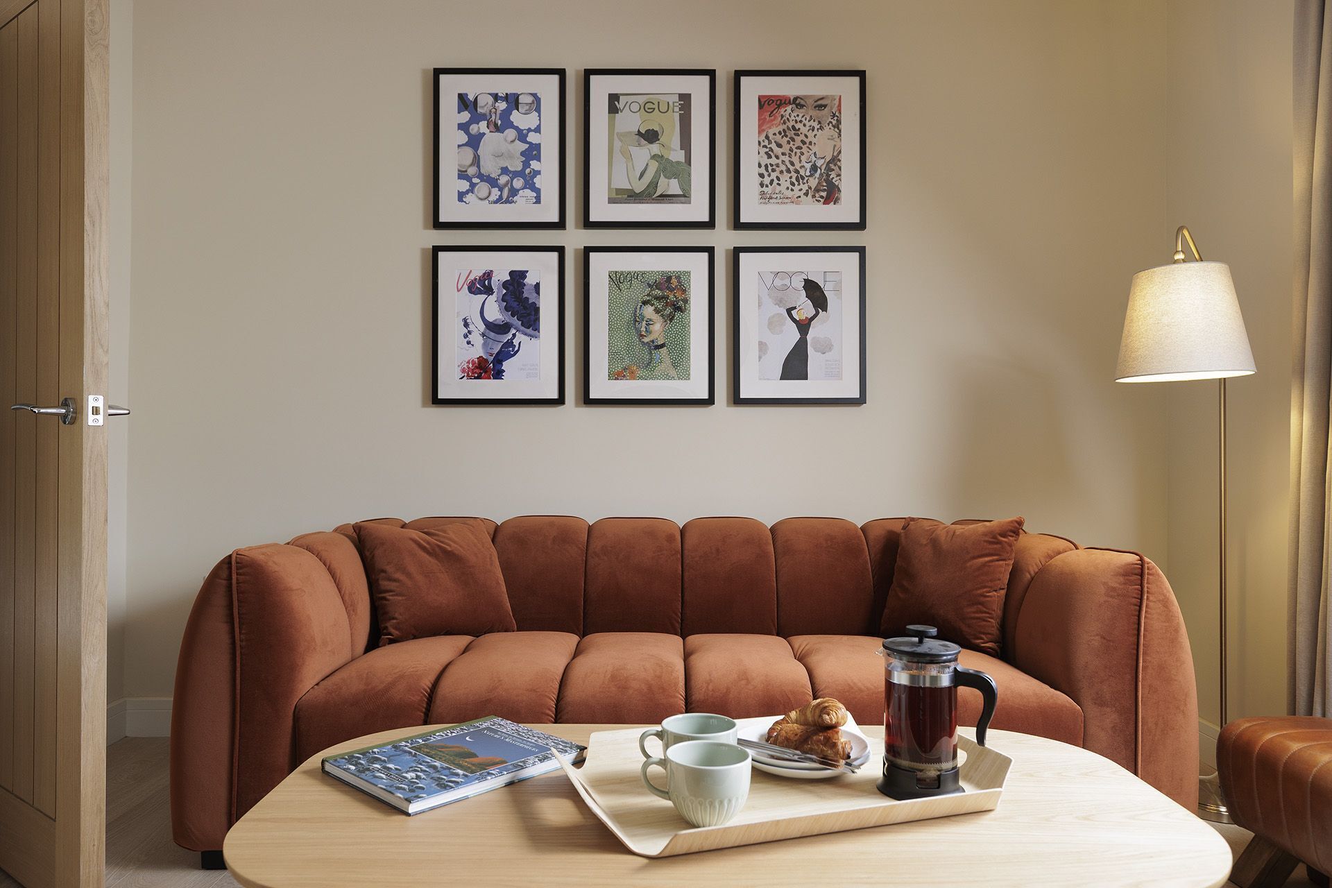 Una habitación con un sofá marrón, una mesita de centro con un libro, dos tazas, un plato con comida y una cafetera.