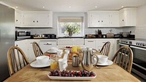 Una cocina moderna con armarios blancos, una mesa de comedor de madera con cosas para el desayuno, y vistas al exterior a través de una ventana.