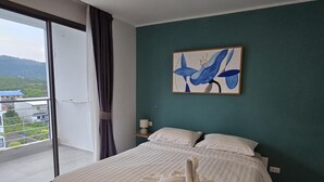 Ein Schlafzimmer mit Bett, einem Gemälde und Blick auf ein Gebäude und Grünflächen.