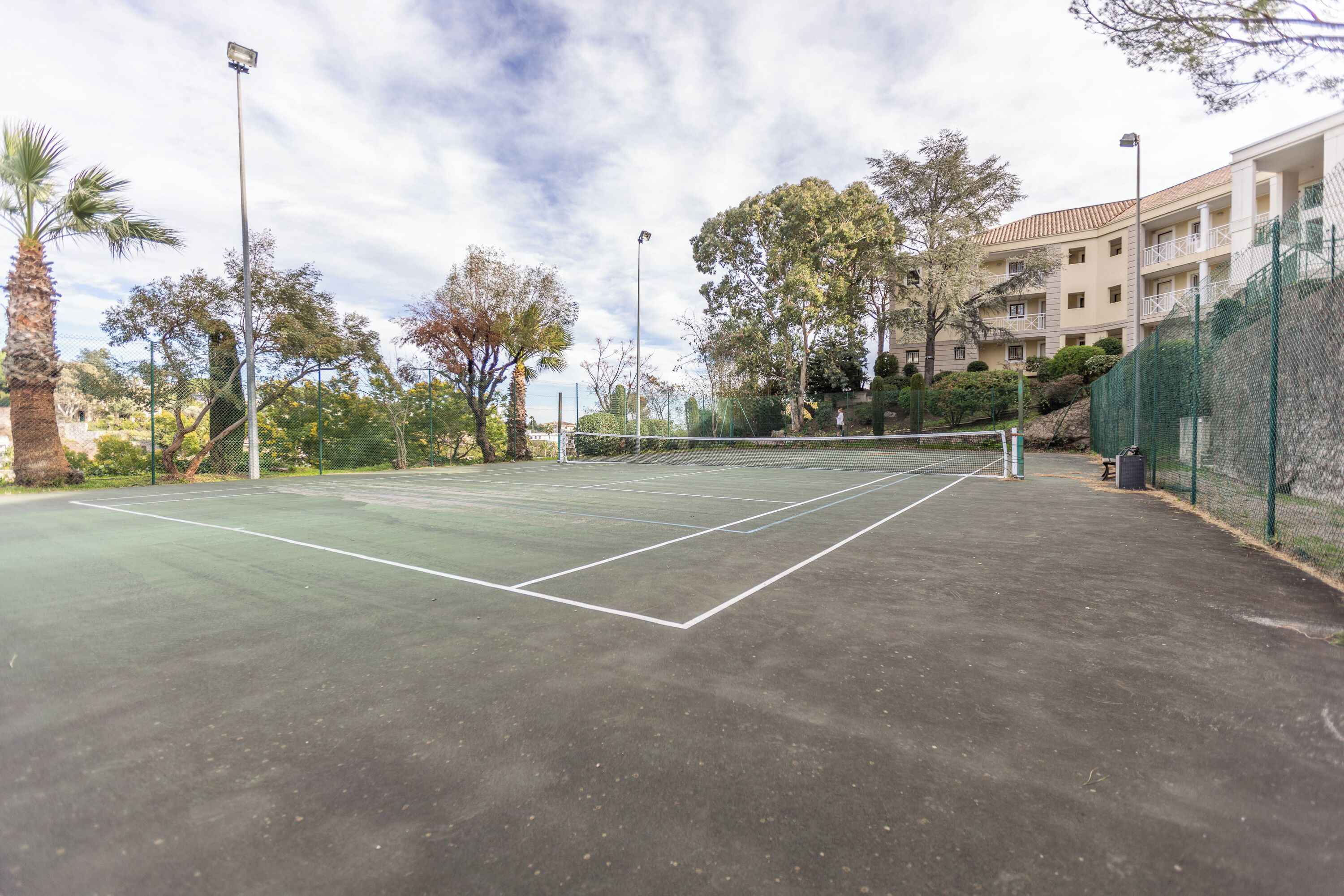 Un court de tennis en plein air, entouré d’arbres et bordé par un bâtiment.
