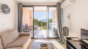 A modern living room with a sofa, a TV, and a balcony with a view. - Bright 1-bedroom sea & mountain view min. from beach (Cannes)