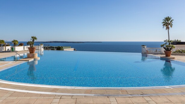 A clear blue infinity pool with a view of the sea, surrounded by potted plants and a white railing. - Bright 1-bedroom sea & mountain view min. from beach (Cannes)