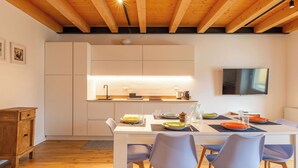 Una cocina moderna con vigas de madera, un televisor montado en la pared y una zona de comedor con sillas y platos.