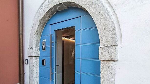 Una puerta azul con cerradura electrónica, un ascensor y un arco de piedra.