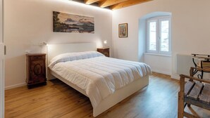 Un dormitorio con techo de madera, una cama con cubrecama blanco, una mesita de noche, una pequeña mesa y una ventana.