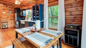 Een houten chalet van binnen met een keuken, eethoek en een groot raam met gordijnen.