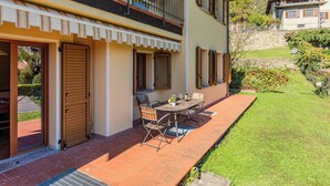 Ein zweistöckiges Gebäude mit einem Balkon, einer Terrasse mit Tisch und Stühlen sowie einem Rasen.