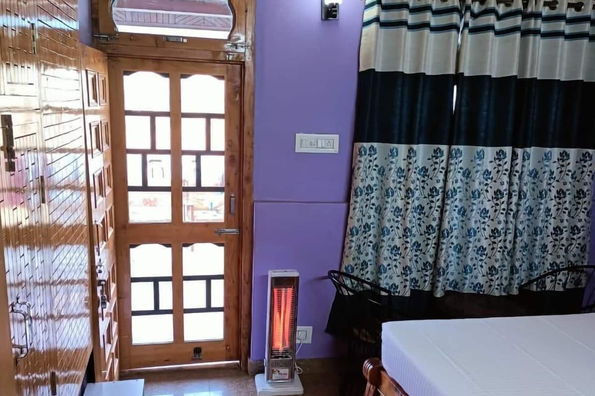 Ein Zimmer mit einem Bett, einem Heizkörper, einem Mülleimer, einem Fenster mit Vorhängen und einer Tür.