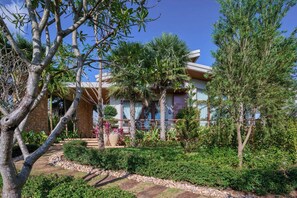 A building with a stone facade, a wooden deck, and a well-maintained garden with various plants and trees.