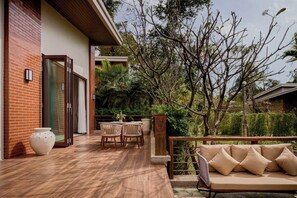 A wooden deck with a sofa and chairs, a brick wall, and a glass door.