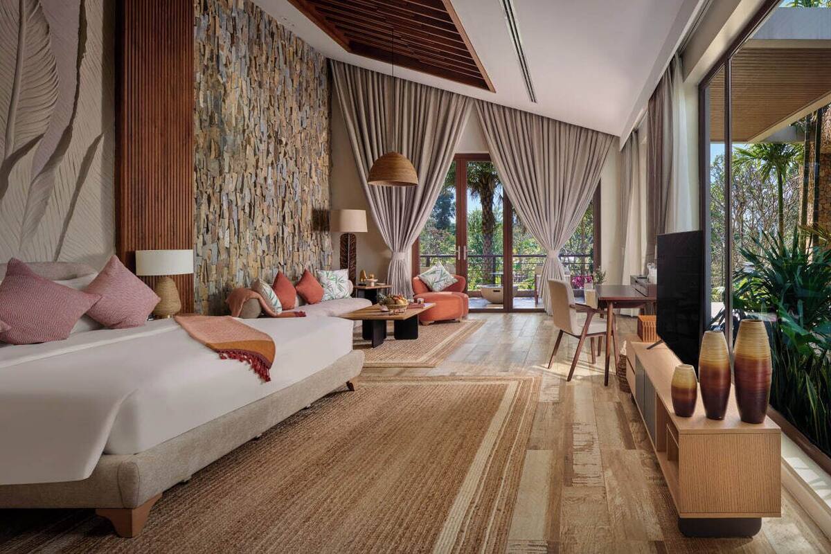 A modern hotel room with a large bed, a sofa, a dining area, and a TV.