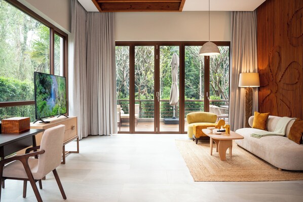 A modern living room with a large TV, a sofa, a yellow armchair, and a dining area with a wooden table and chairs. - Samanea Wellness Resort (Veal Veaeng)