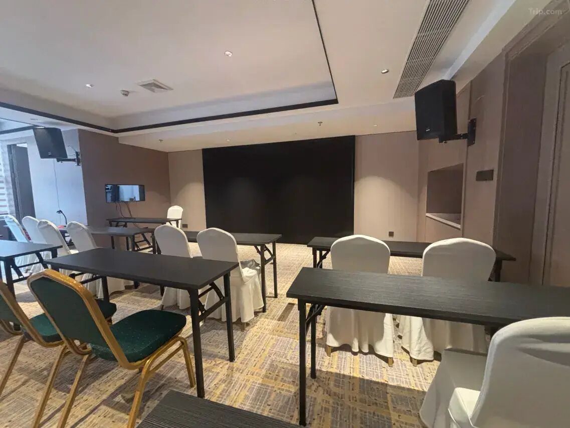 A conference room with tables and chairs, a large screen, and speakers on the walls.