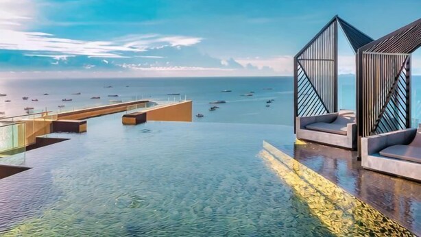 A infinity pool with a view of the sea and boats, modern seating areas, and a clear sky. - EDGE Central holiday in pattaya (Pattaya)