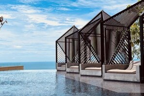 Un espace amĂ©nagĂ© au bord de la piscine, avec vue sur lâocĂ©an, une structure en bois dotĂ©e de siĂšges et un ciel dĂ©gagĂ©.