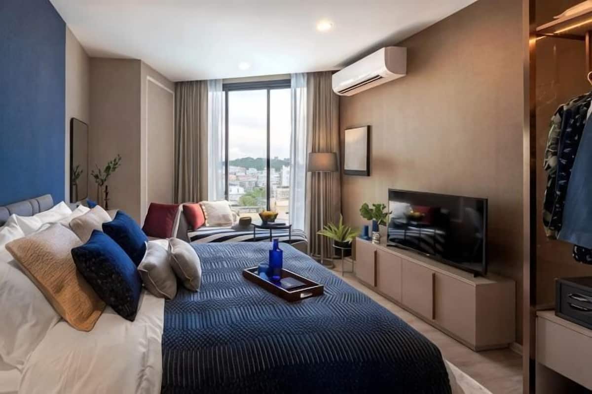 A hotel room with a bed, TV, and a view of the city.