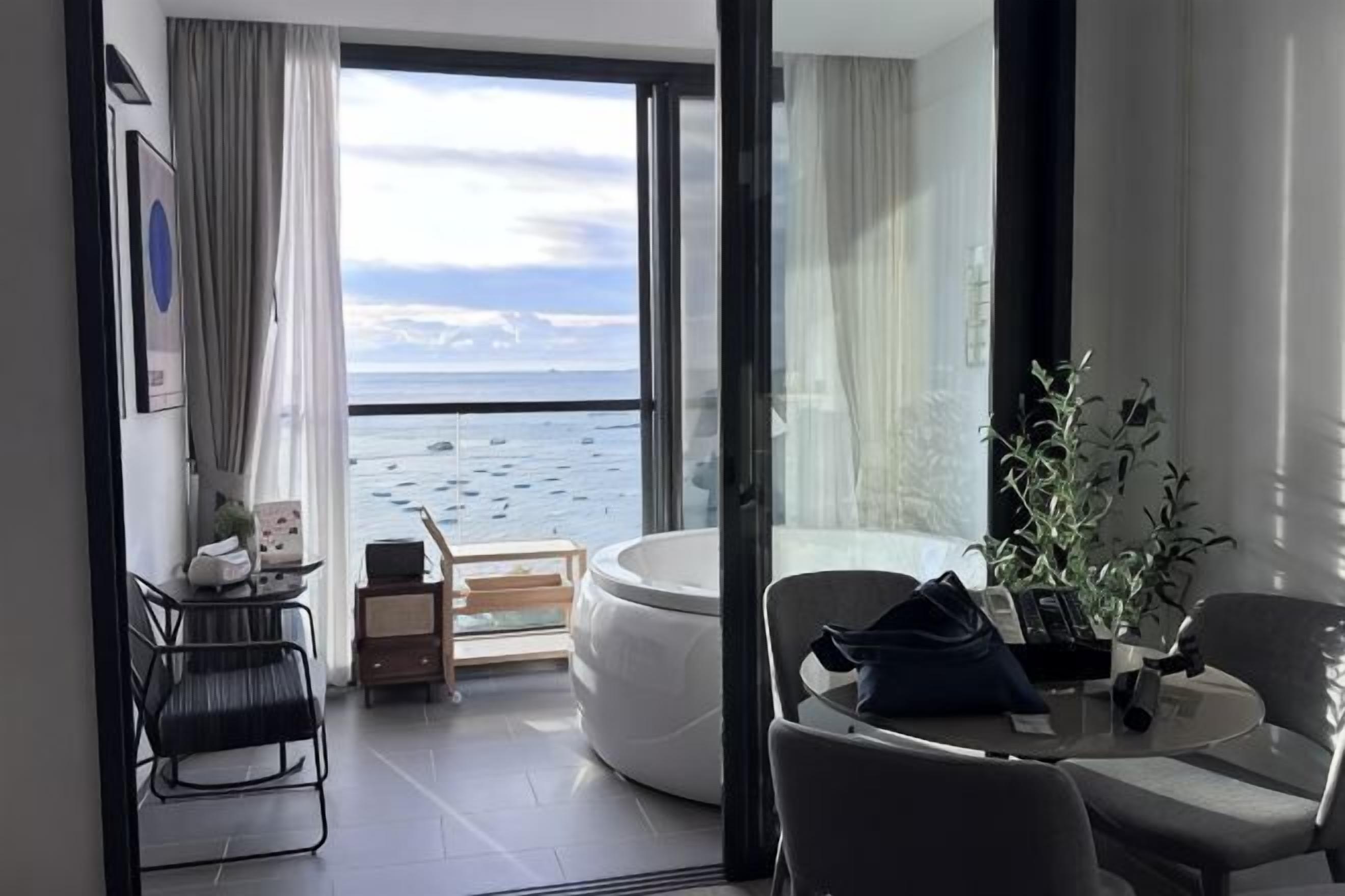A room with a view of the sea, a seating area, and a small table with a plant.