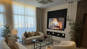 Een moderne woonkamer met een bank, fauteuils, een salontafel en een televisie die boven een open haard is bevestigd.