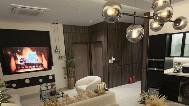 Een moderne woonkamer met een flatscreen televisie, een open haard, een eettafel met placemats en een keuken in de achtergrond.
