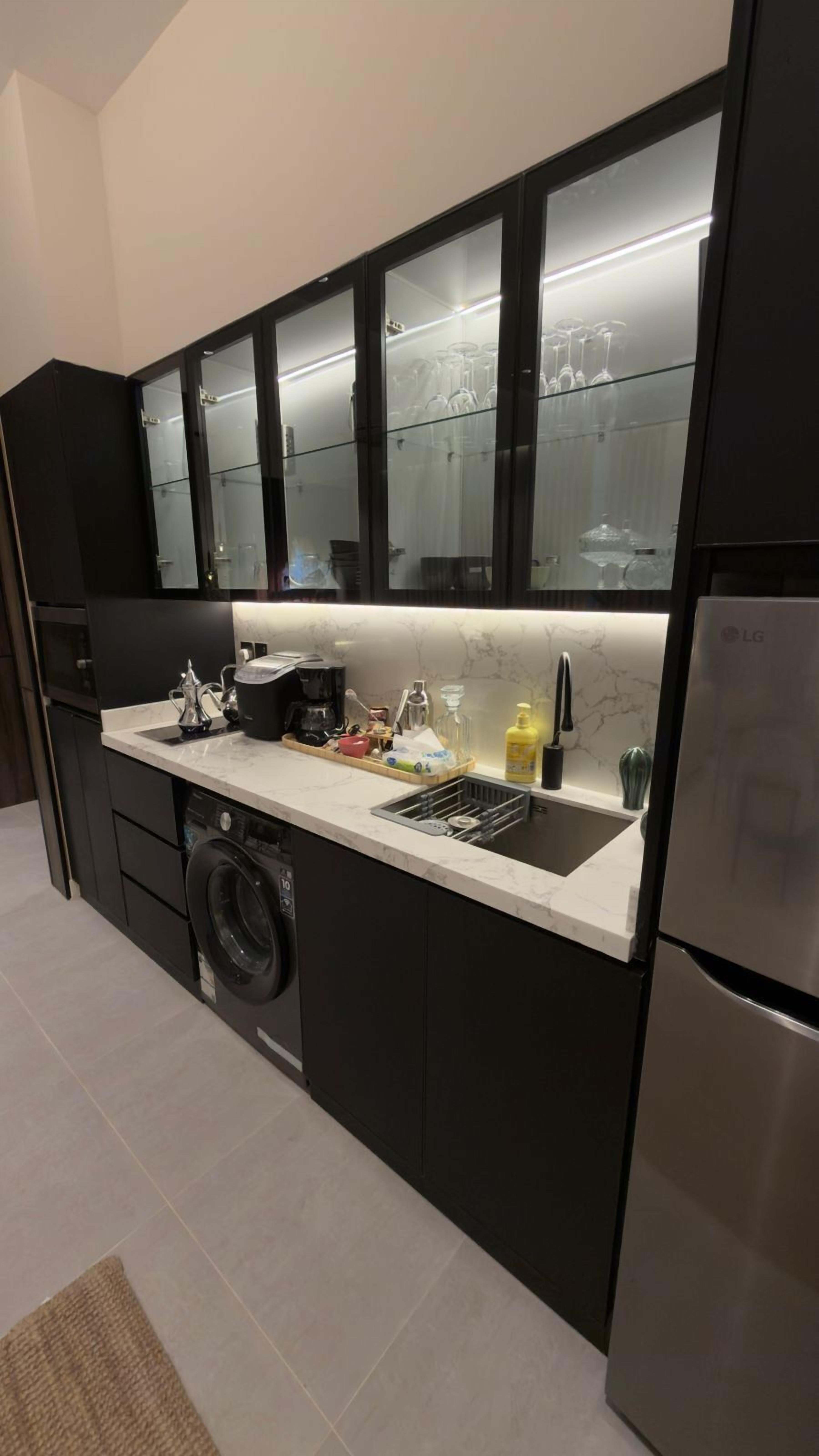 A modern kitchen with a built-in washing machine, a stainless steel refrigerator, and a glass-fronted cabinet above the sink.