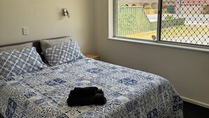 A bedroom with a bed, a ceiling fan, a window with a view of the outside, and an air conditioning unit.