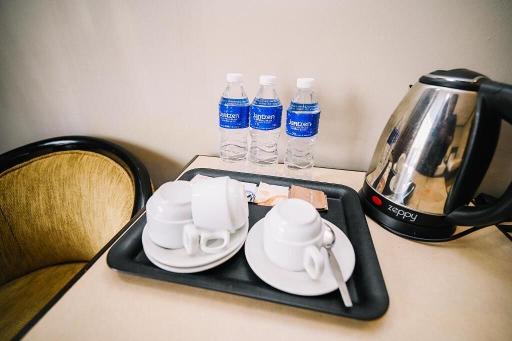 Una bandeja con dos tazas blancas, una cuchara y tres botellas de agua sobre una mesa.
